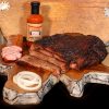 Cooper's Old Time Pit Bar-b-que mail order taster box includes brisket, pork tenderloin, and a bottle of bbq sauce. Displayed on a beautiful cutting board arrangement with garnishes.